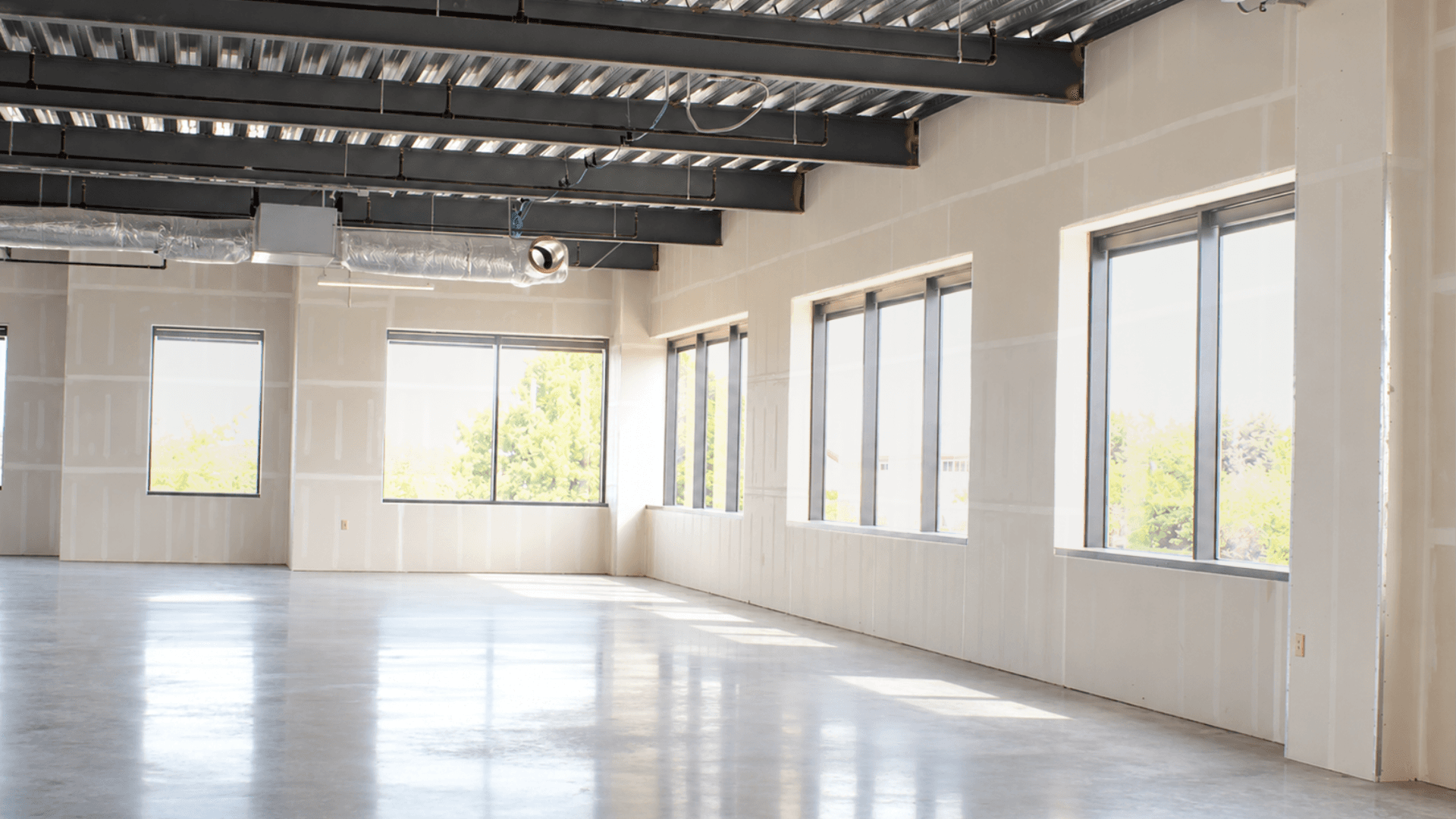 Commercial interior nearing completion with exposed steel beams, ductwork, unfinished drywall, and polished concrete floors